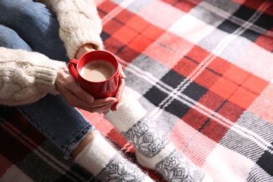 Woman relaxing with cup of hot winter drink on checkered plaid, closeup. Space for text