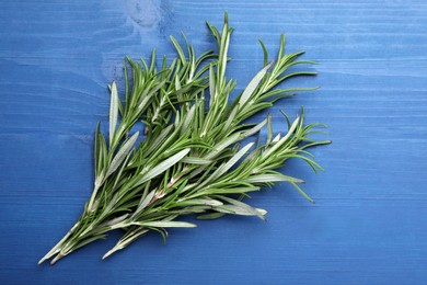 Photo of Sprigs of fresh rosemary on blue wooden table, top view