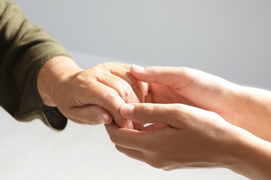 Photo of Helping hands on grey background, closeup. Elderly care concept