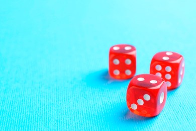 Photo of Three red game dices on light blue background, closeup. Space for text