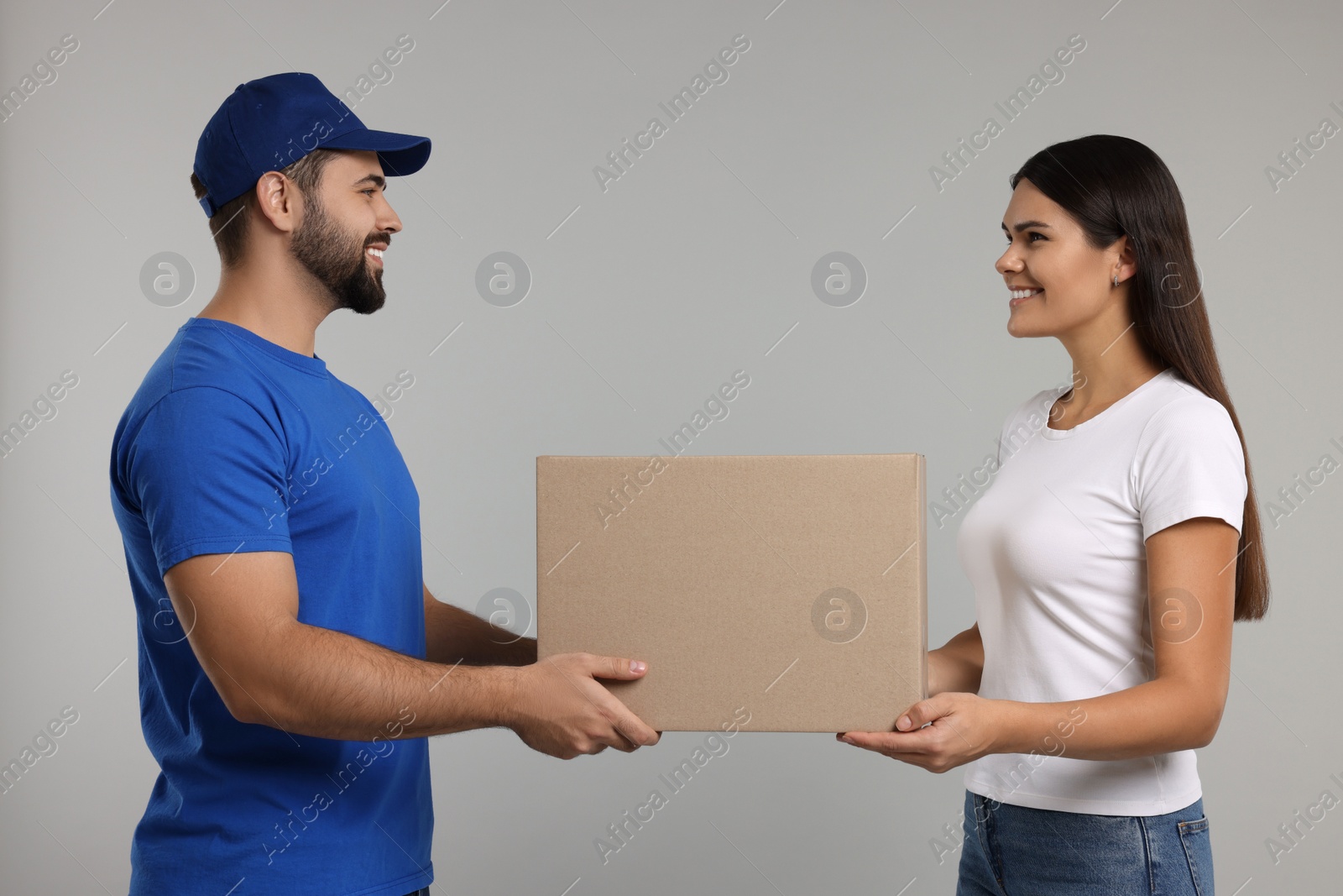 Photo of Smiling courier giving parcel to receiver on grey background