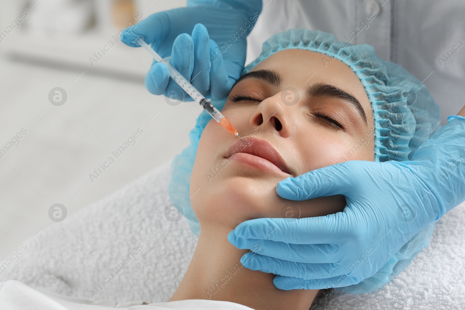 Photo of Doctor giving lips injection to young woman in clinic, closeup. Cosmetic surgery