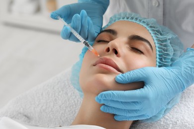 Doctor giving lips injection to young woman in clinic, closeup. Cosmetic surgery