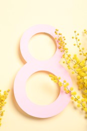 Photo of 8 March greeting card design with mimosa flowers on light yellow background, top view