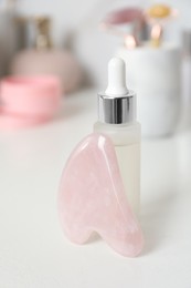 Photo of Rose quartz gua sha tool and cosmetic product on white table, closeup