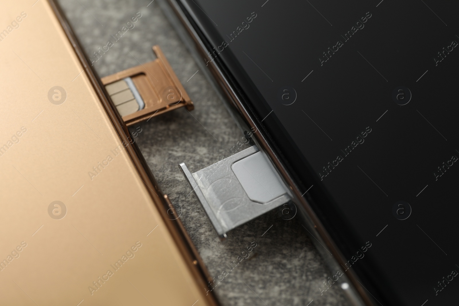 Photo of Mobile phones with Sim cards in trays on grey table, closeup