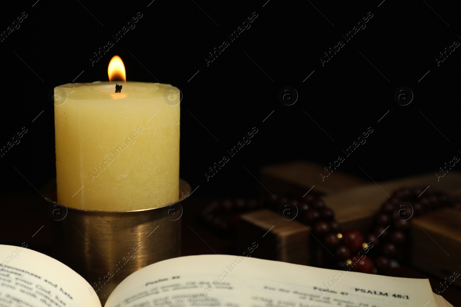 Photo of Church candle, Bible, wooden cross and rosary beads on table, closeup. Space for text