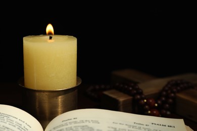 Church candle, Bible, wooden cross and rosary beads on table, closeup. Space for text