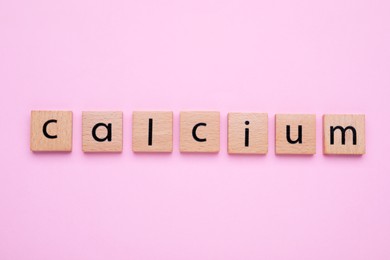 Photo of Word Calcium made of wooden cubes with letters on pale pink background, top view