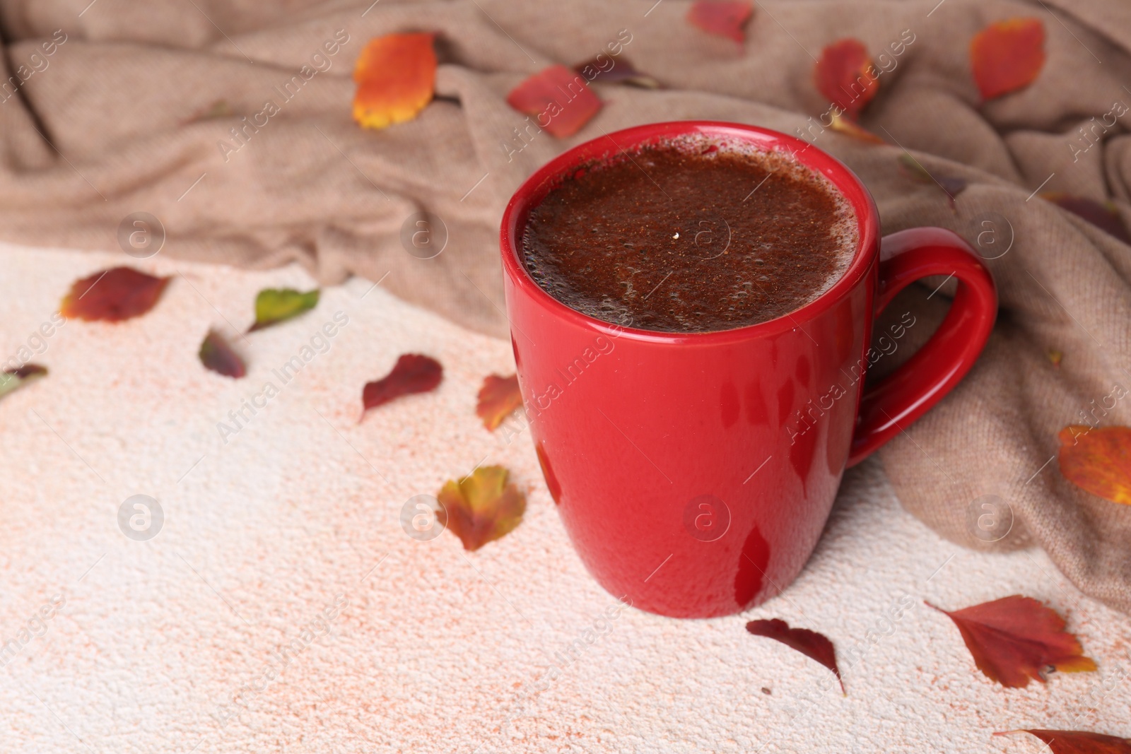 Photo of Cup of hot drink, leaves and soft knitted fabric on beige textured table, closeup with space for text. Cozy autumn atmosphere