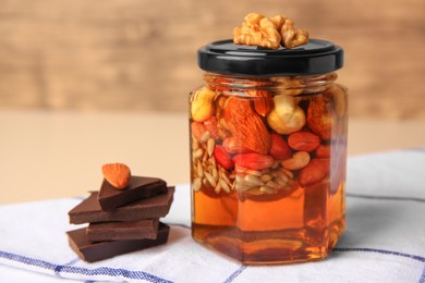 Different nuts and honey in jar, chocolate on table, closeup