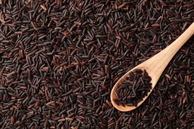 Photo of Wooden spoon with cereal on raw brown rice, top view. Space for text