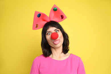 Photo of Funny woman with large bow and clown nose on yellow background. April fool's day