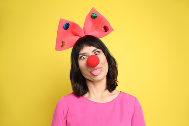 Funny woman with large bow and clown nose on yellow background. April fool's day