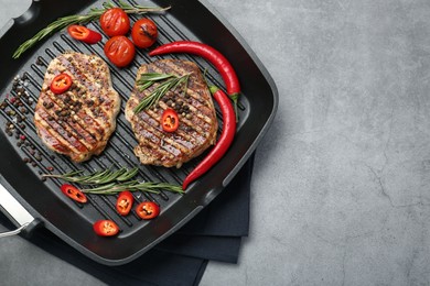 Photo of Grill pan with delicious pork steaks, spices and vegetables on grey table, top view. Space for text