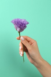 Photo of Woman with white polish on nails holding flower against green background, closeup