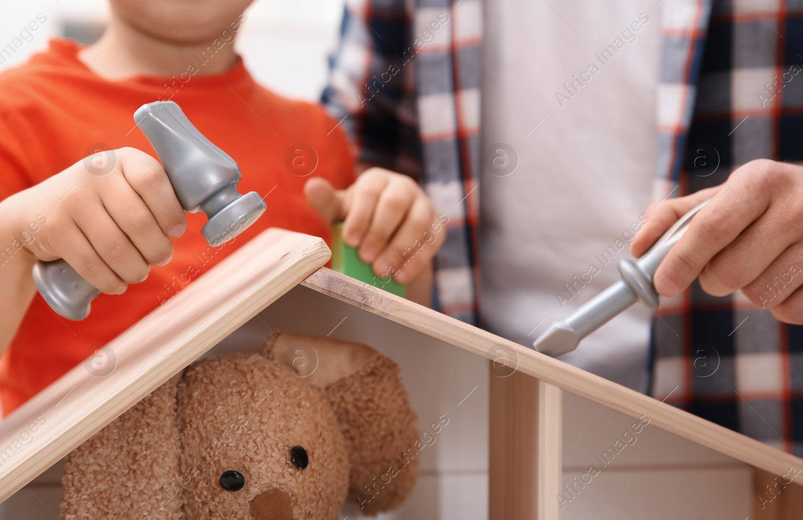 Photo of Man and his child playing builders with wooden doll house at home, closeup