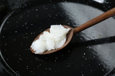 Frying pan with organic coconut cooking oil and wooden spoon, closeup