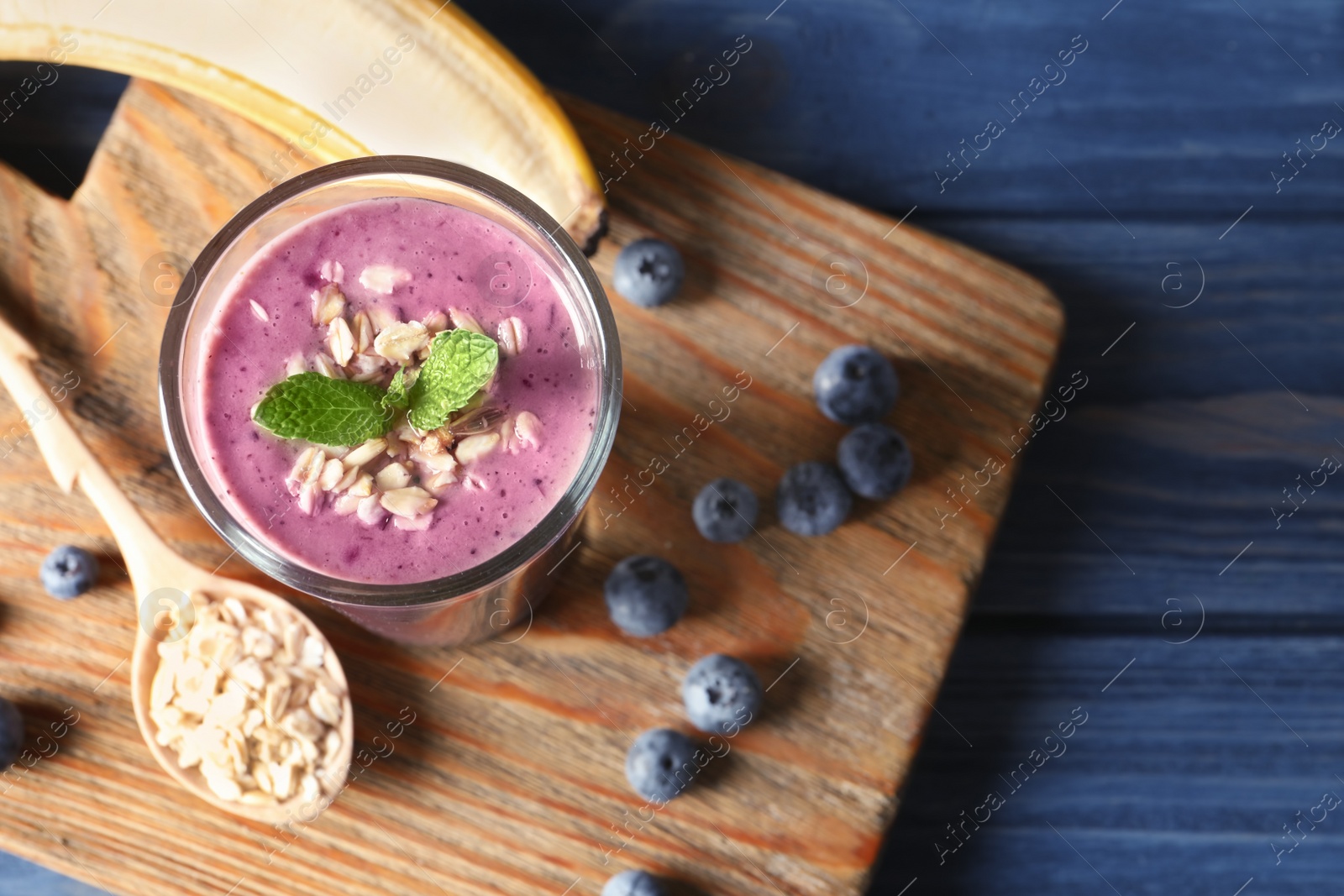 Photo of Glass of blueberry smoothie with oatmeal on wooden table, top view