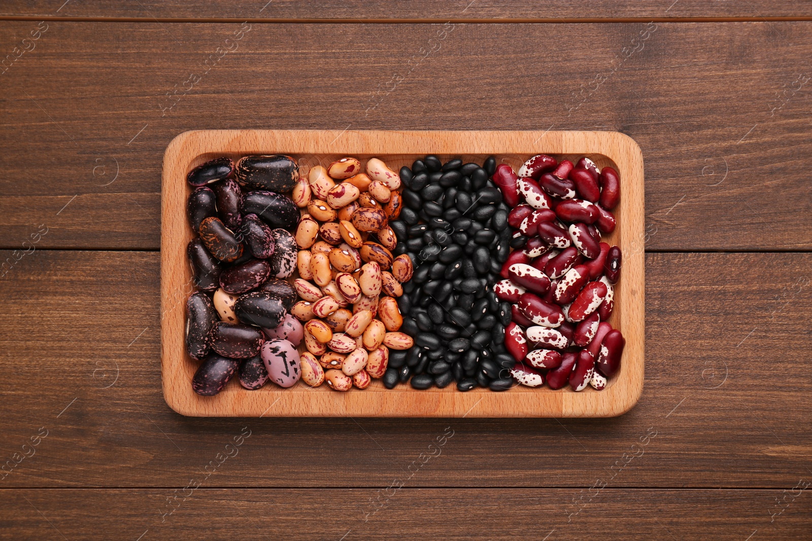 Photo of Plate with different kinds of dry kidney beans on wooden table, top view