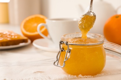 Spoon with delicious orange marmalade over jar on table. Space for text