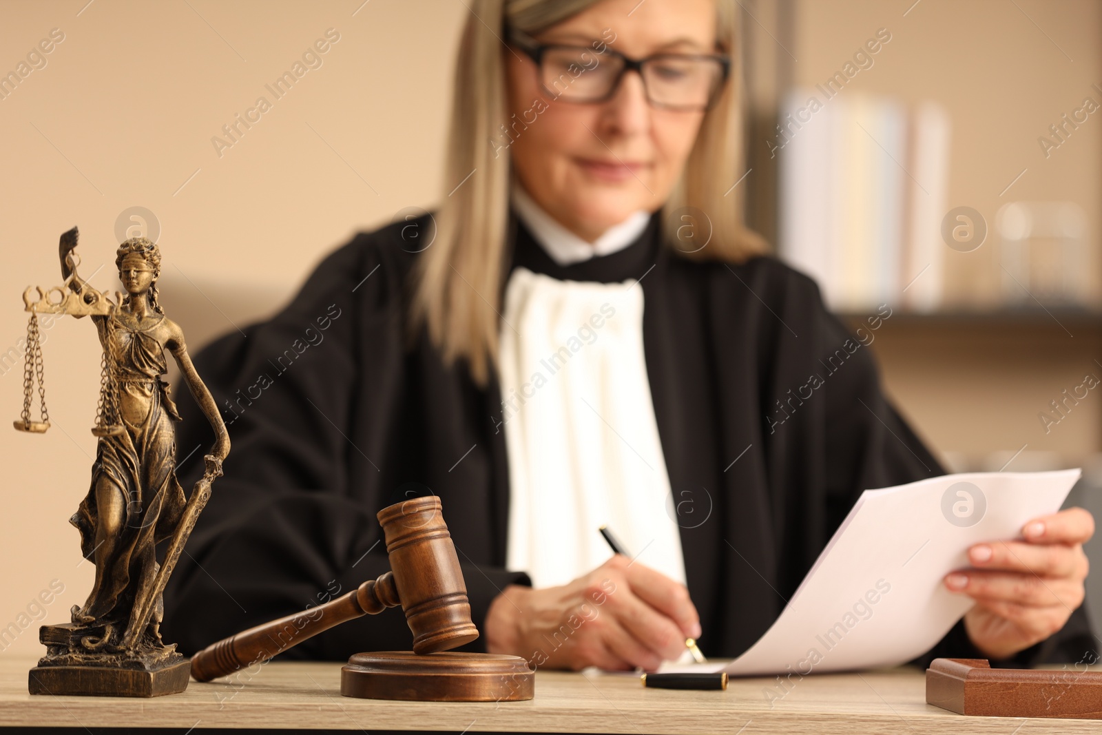 Photo of Judge working indoors, selective focus. Figure of Lady Justice and mallet on wooden table