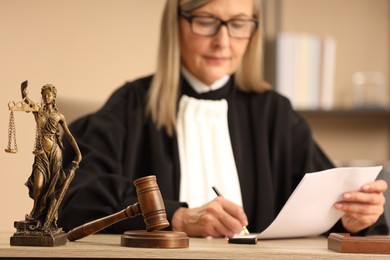 Judge working indoors, selective focus. Figure of Lady Justice and mallet on wooden table