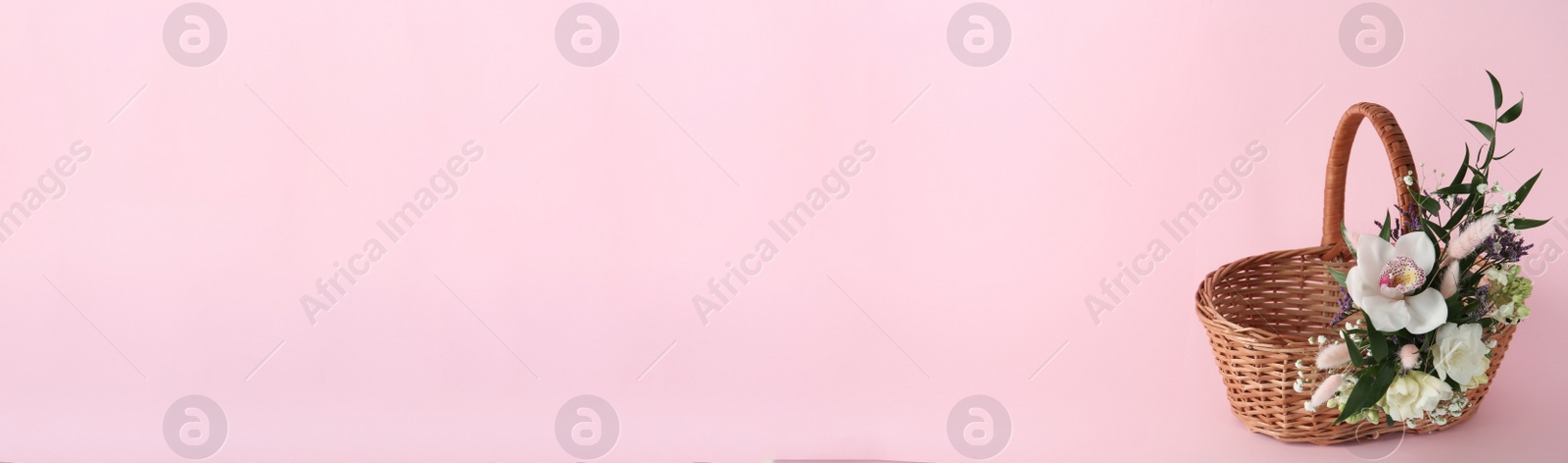 Photo of Wicker basket decorated with beautiful flowers on pink background, space for text. Easter item