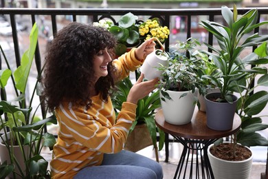 Beautiful young woman watering green houseplants on balcony