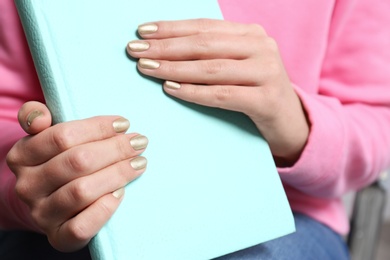 Photo of Woman with gold manicure holding notebook, closeup. Nail polish trends