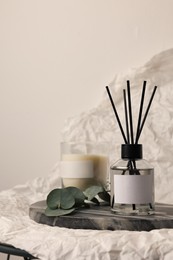 Photo of Aromatic reed air freshener, eucalyptus leaves and candle on white crumpled paper, space for text