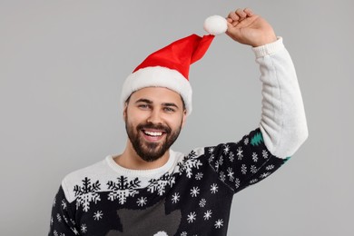 Photo of Happy young man in Christmas sweater and Santa hat on grey background