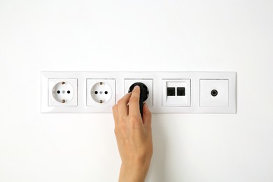 Woman putting plug into socket indoors, closeup