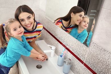 Happy mother and daughter washing hands in bathroom at home