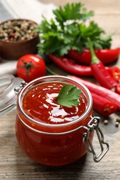 Photo of Spicy chili sauce in glass jar on wooden table, closeup