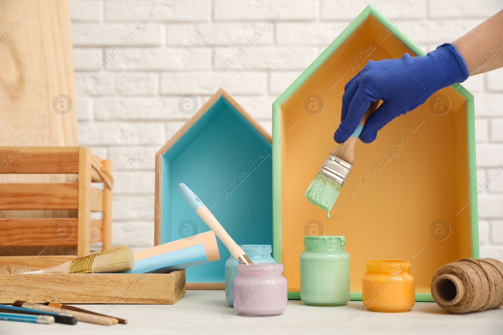 Photo of Decorator dipping brush into jar of green paint at white table, closeup