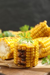 Delicious grilled corn cobs on wooden table, closeup