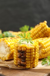 Photo of Delicious grilled corn cobs on wooden table, closeup