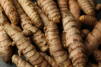 Many raw turmeric roots on black textured table, closeup