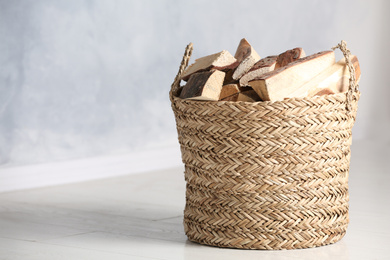 Photo of Wicker basket with cut firewood on white floor indoors. Space for text