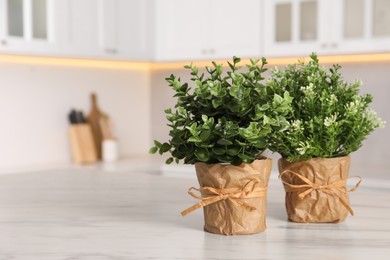 Photo of Artificial potted herbs on white marble table in kitchen, space for text. Home decor