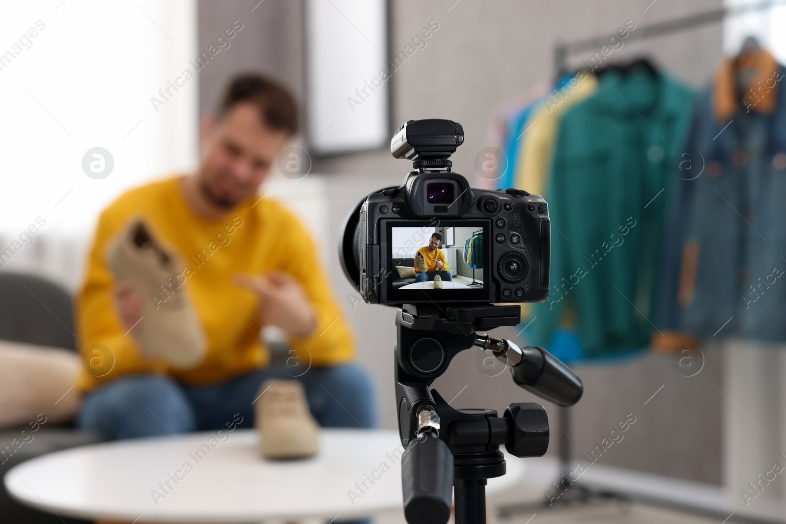 Photo of Fashion blogger showing shoes while recording video at home, focus on camera