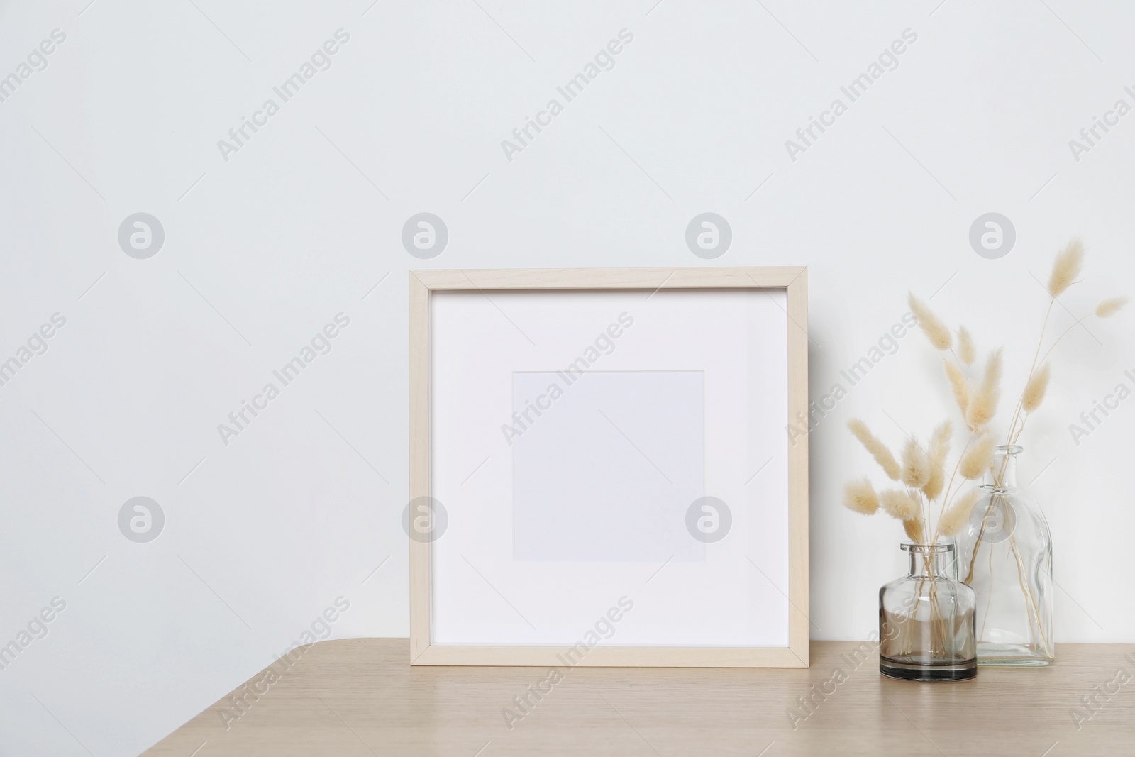 Photo of Empty photo frame and vases with dry decorative spikes on wooden table. Mockup for design