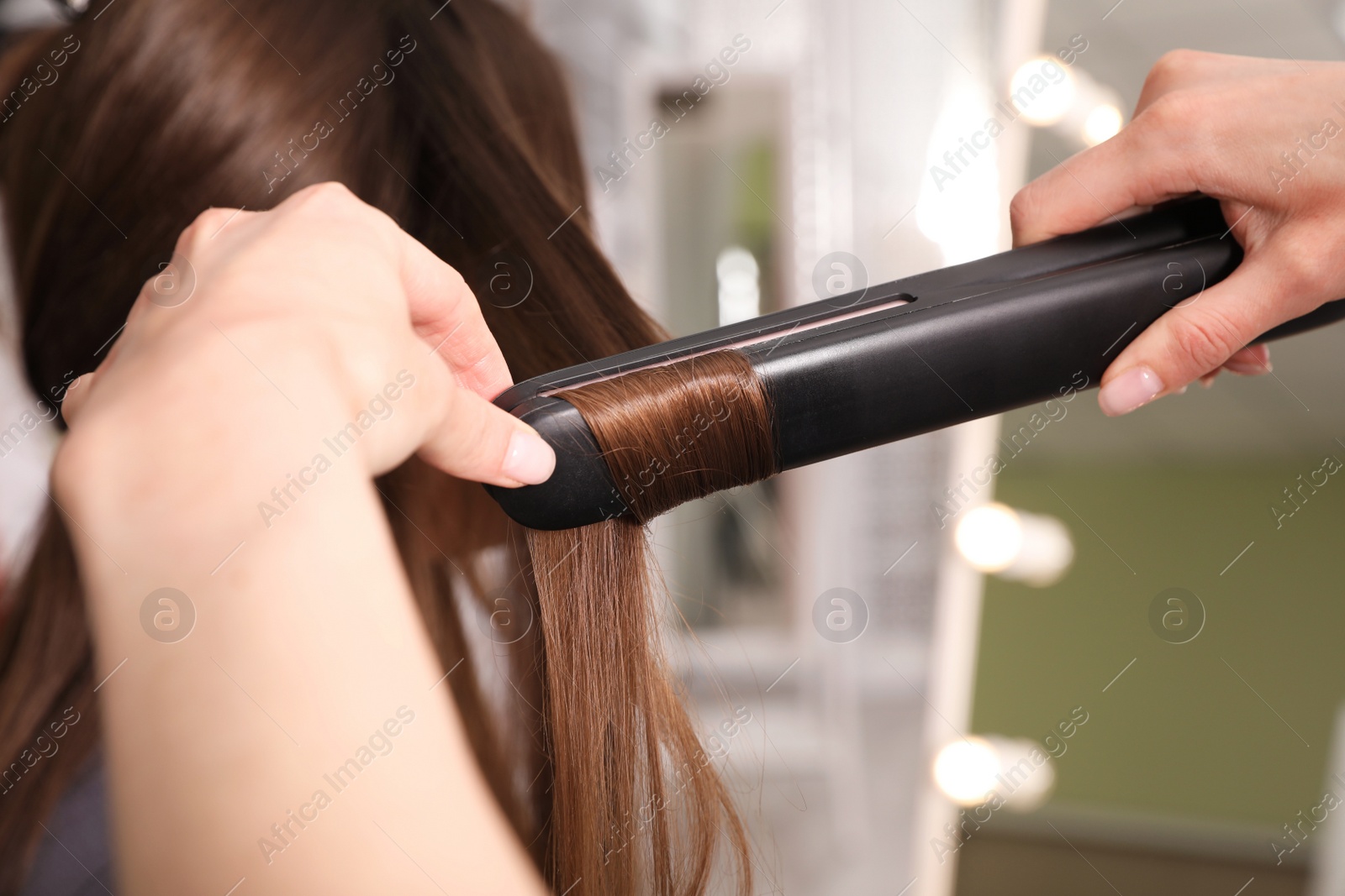 Photo of Stylist curling woman's hair with flat iron in salon