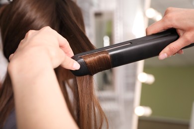 Photo of Stylist curling woman's hair with flat iron in salon