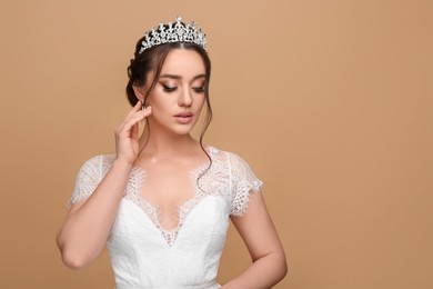 Beautiful young woman wearing luxurious tiara on beige background, space for text