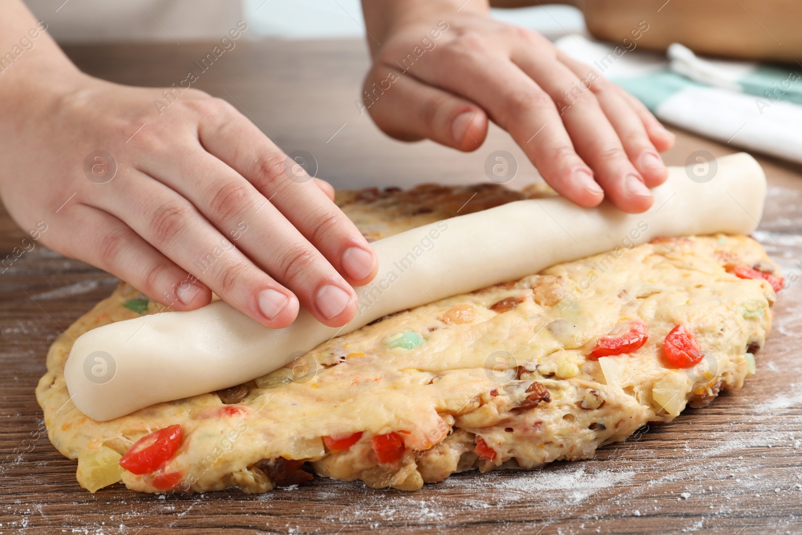 Photo of Woman putting marzipan into raw dough for Stollen at wooden table, closeup. Baking traditional German Christmas bread