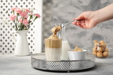 Photo of Woman pouring cream for dalgona coffee into glass at light grey table, closeup