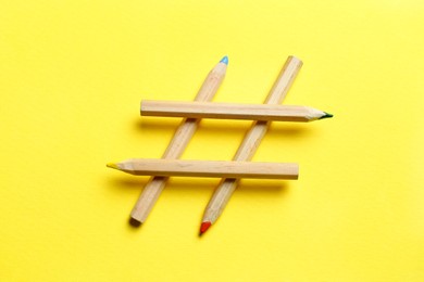 Photo of Hashtag symbol made of wooden pencils on yellow background, top view