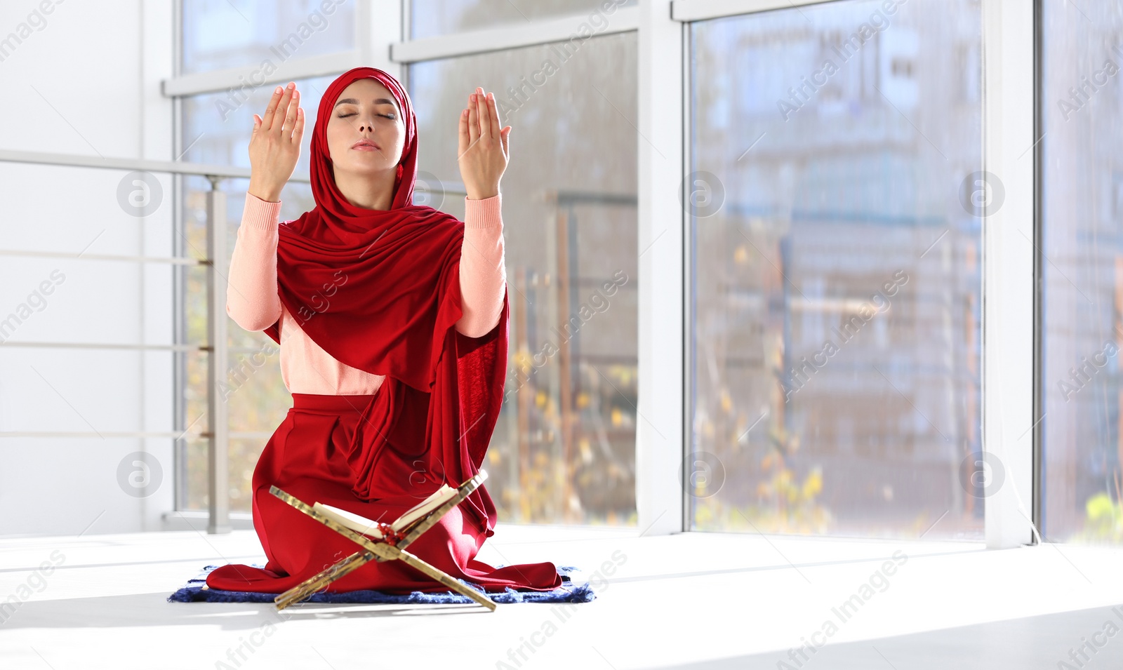 Photo of Muslim woman in hijab praying on mat indoors. Space for text